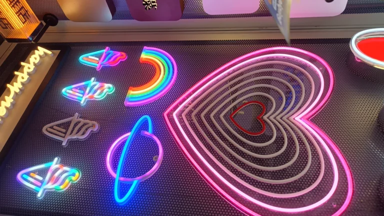 Illuminated rainbow, heart and planet outline samples displayed on a perforated wall.