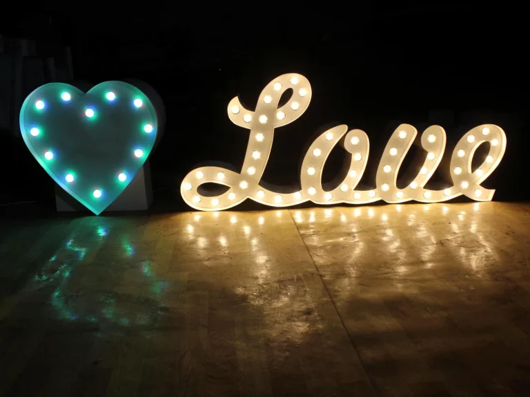 Illuminated script Love letters beside a heart-shaped bulb sign on a dark floor.