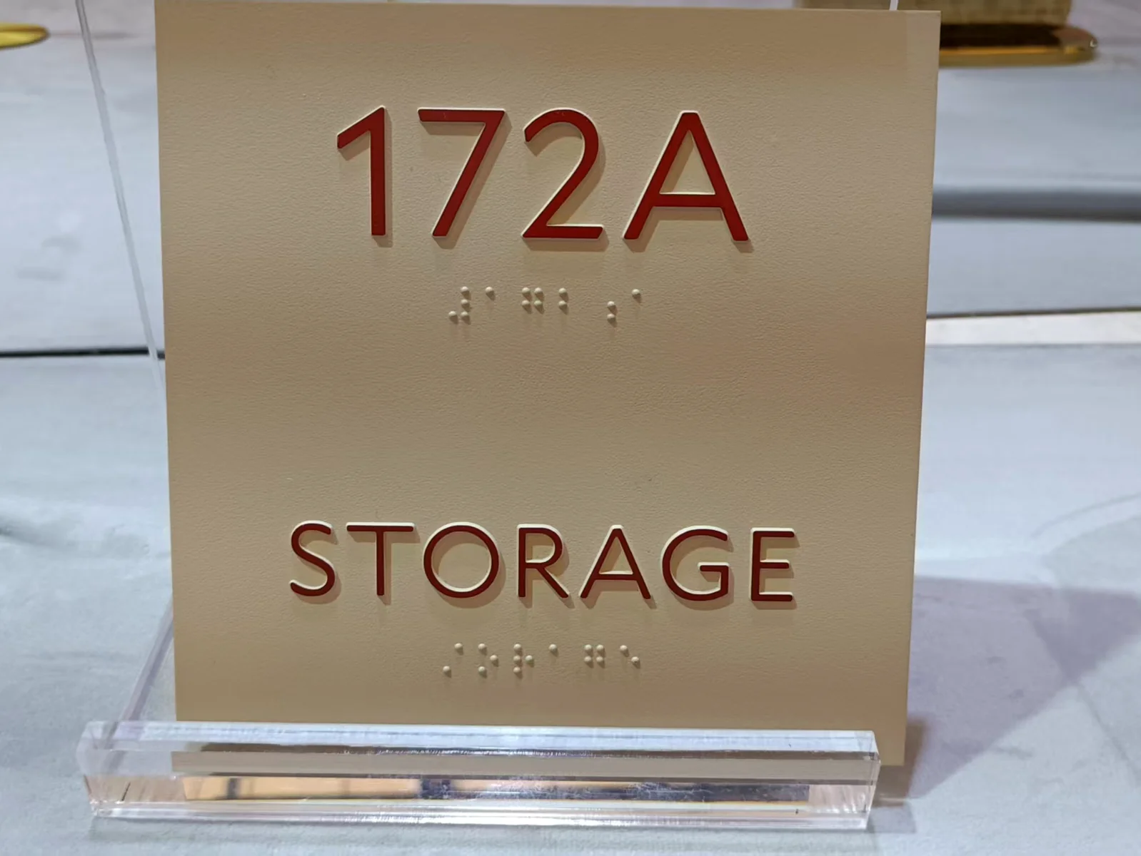 A rectangular sign sample displaying the room code 172A and the word STORAGE, with raised dots below the text.