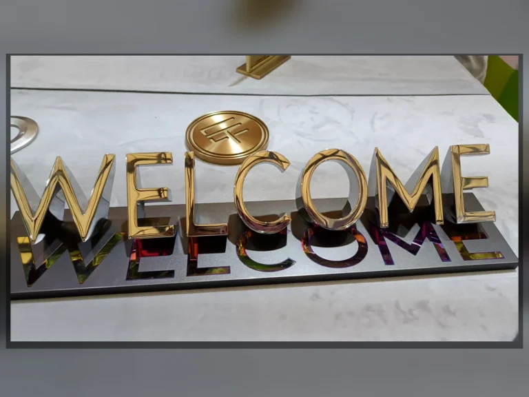 Gold-toned WELCOME letters and a round symbol displayed on a reflective dark base.