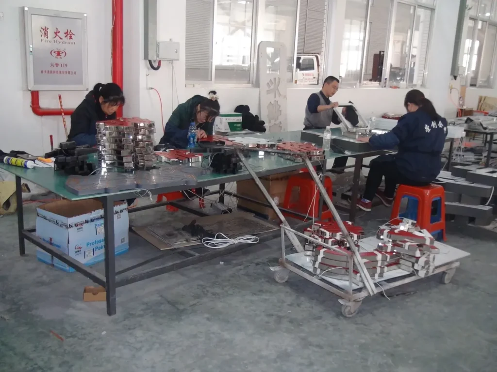 Workers assembling sign letters with wiring visible at the worktables
