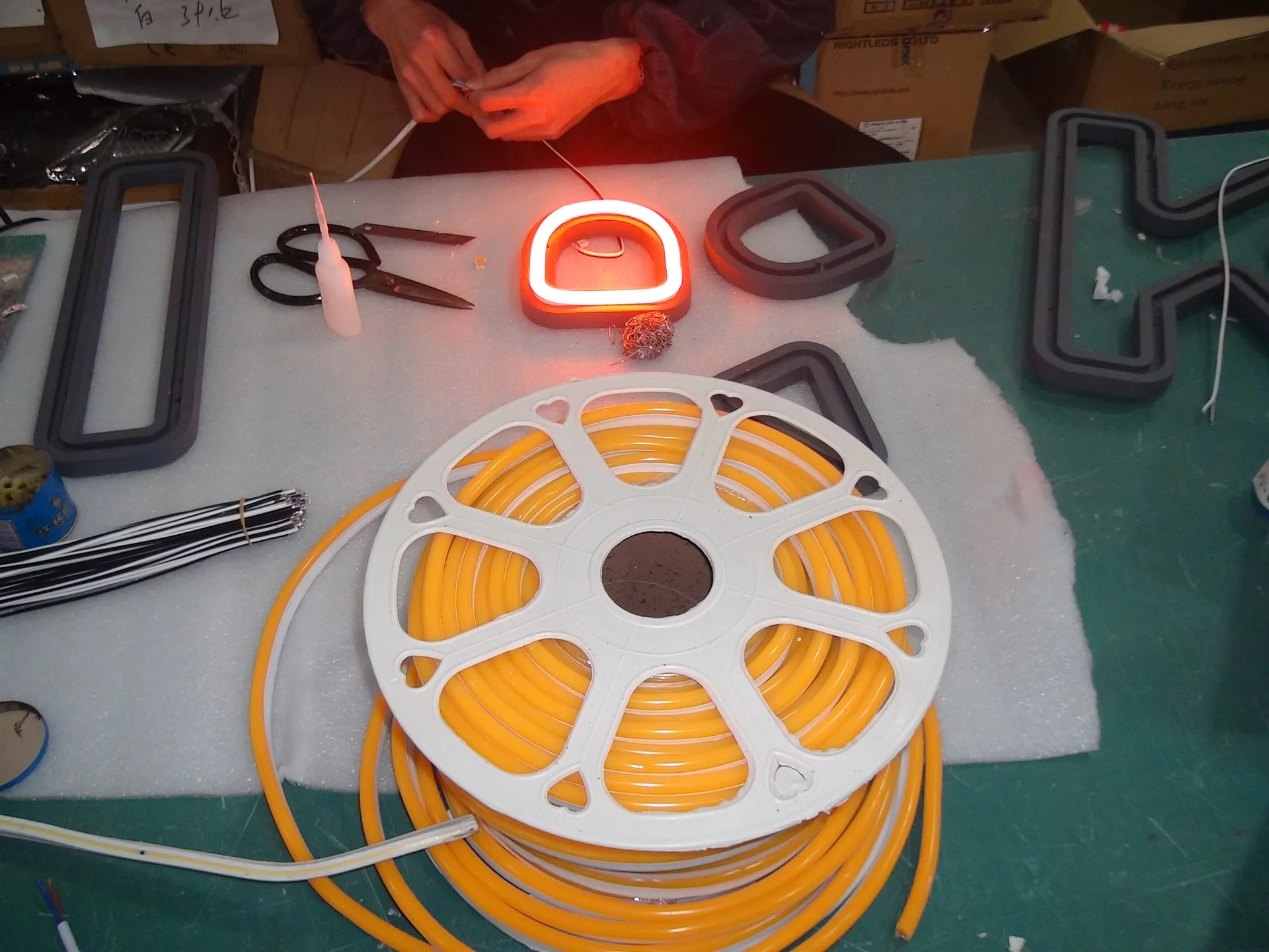 Illuminated neon flex sample beside a reel on a workbench