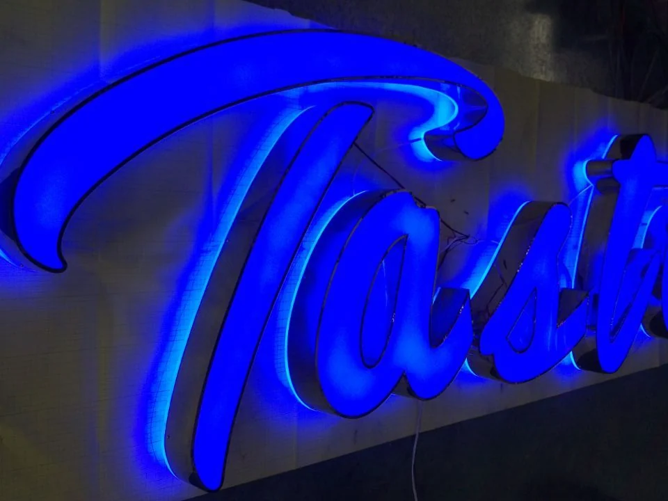 Connected script letters with blue illumination mounted against a wall.