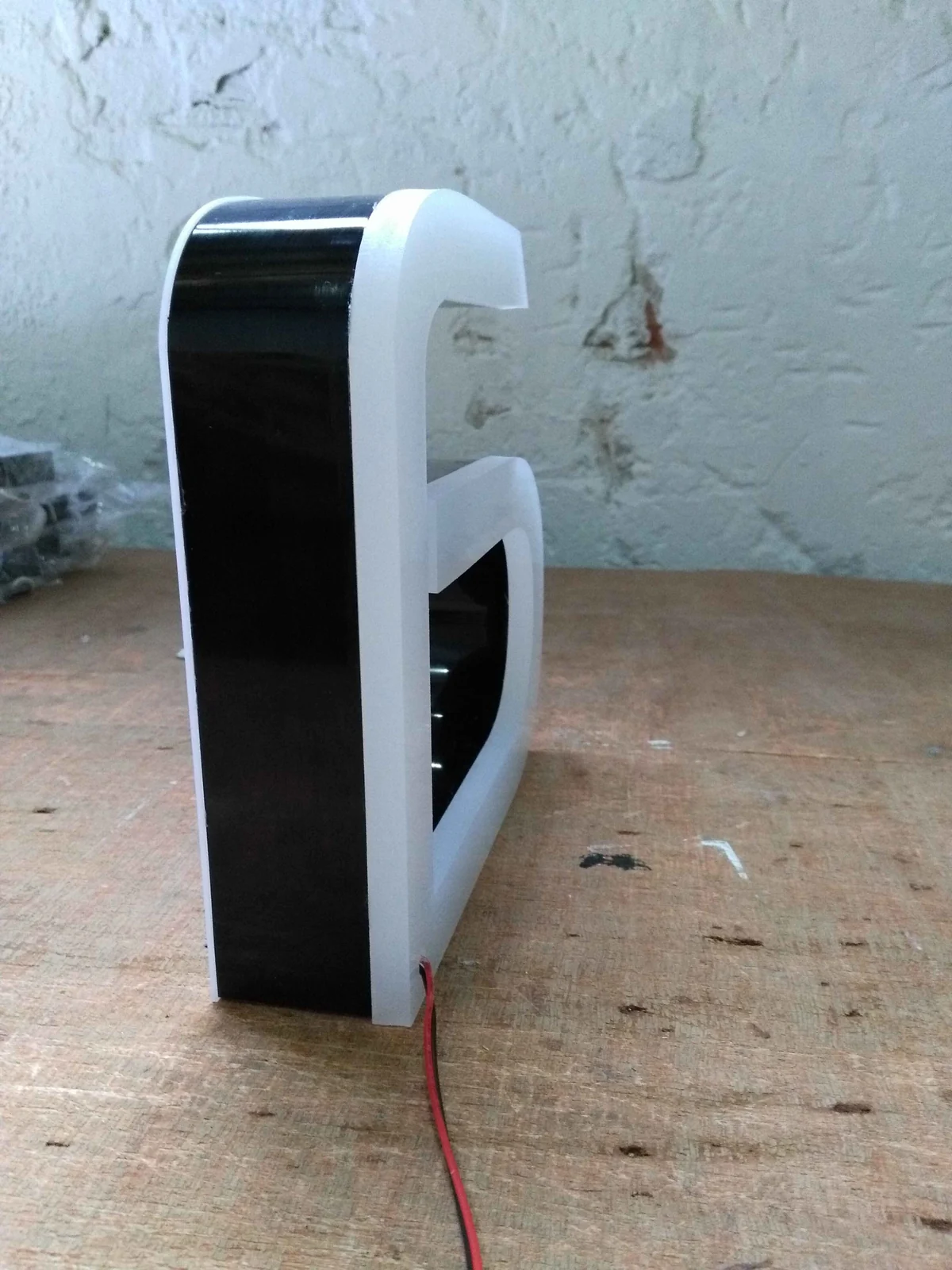 A compact white-faced letter standing on a workbench with a black side return and trailing cable.