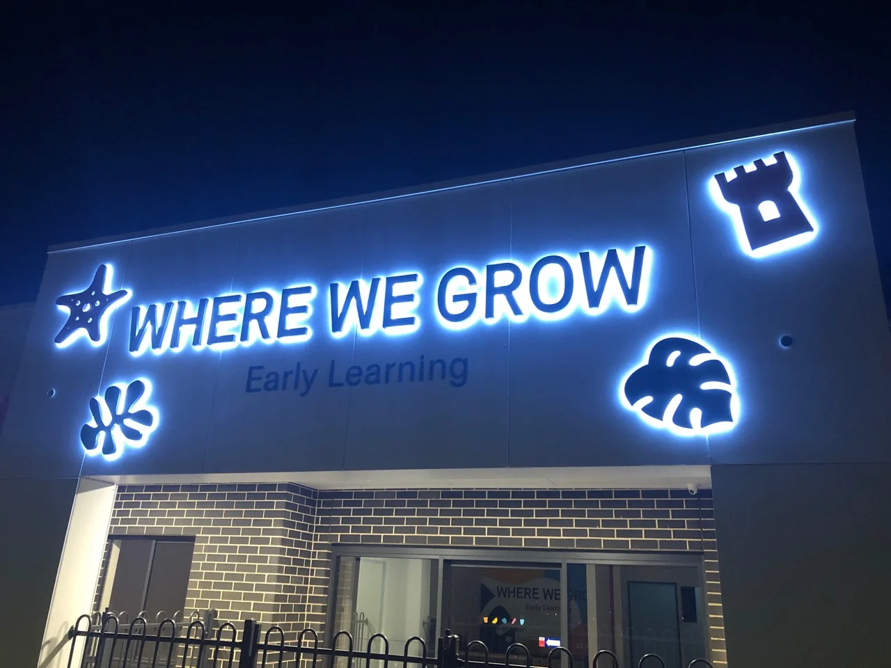 Illuminated letters and symbols mounted above a commercial building entrance at night