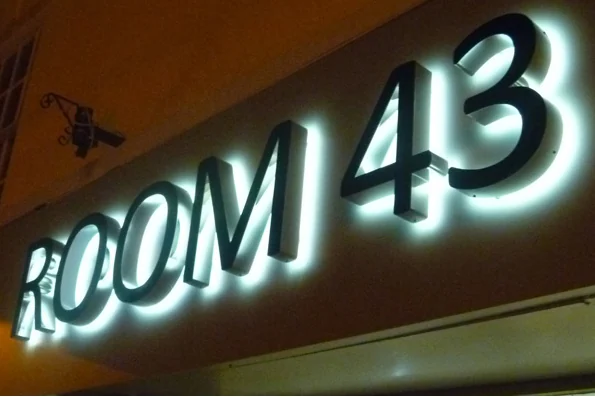 Dark-faced dimensional ROOM 43 letters and numerals with white light around their edges on an interior wall.