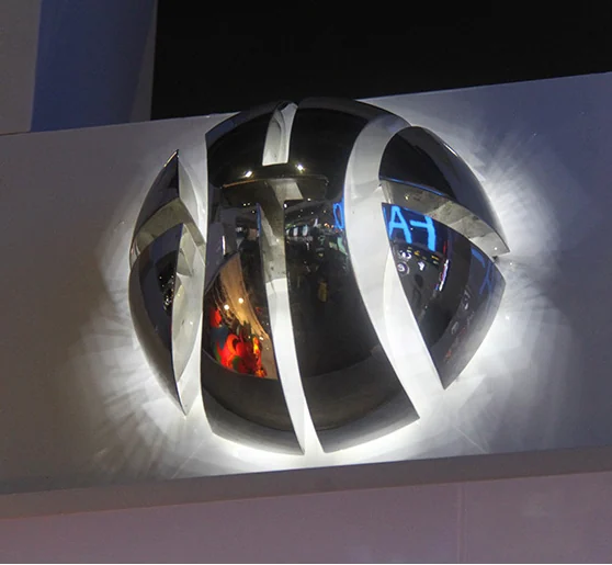 A sculptural rounded logo made from curved reflective sections with white light around its outline.