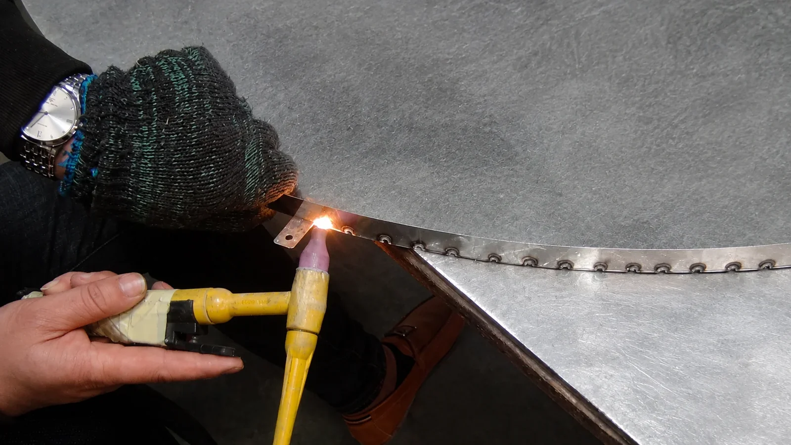 Close view of a technician joining a seam along a shaped metal component.