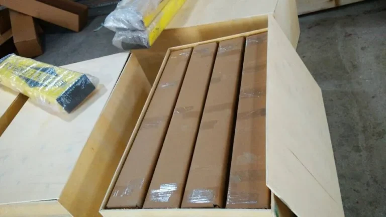 An open wooden crate holding several long cardboard boxes arranged side by side.
