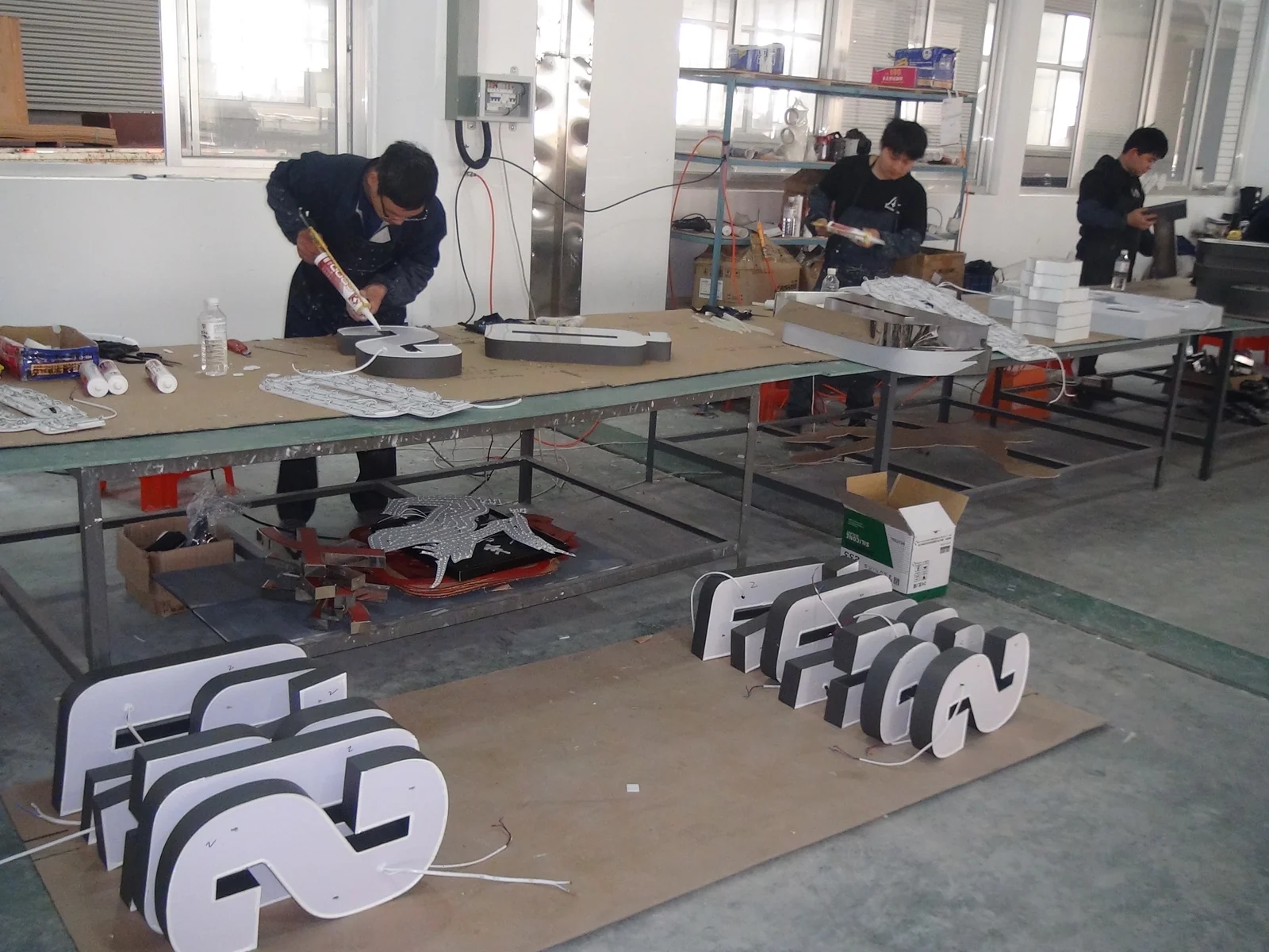 Technicians working at assembly tables with dimensional sign components in the foreground.