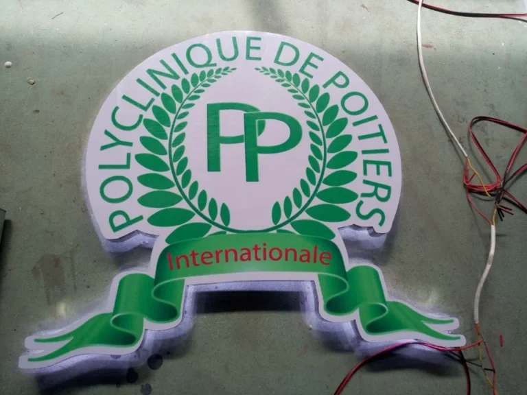 A crest-shaped illuminated sign sample with green lettering and a ribbon-shaped lower section.
