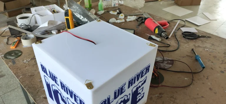 A cube-shaped sign cabinet with lettering on two visible faces on a workbench.