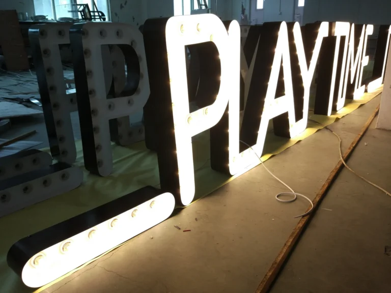 Illuminated PLAYTIME letter bodies with dark returns and loose white leads beside the display.