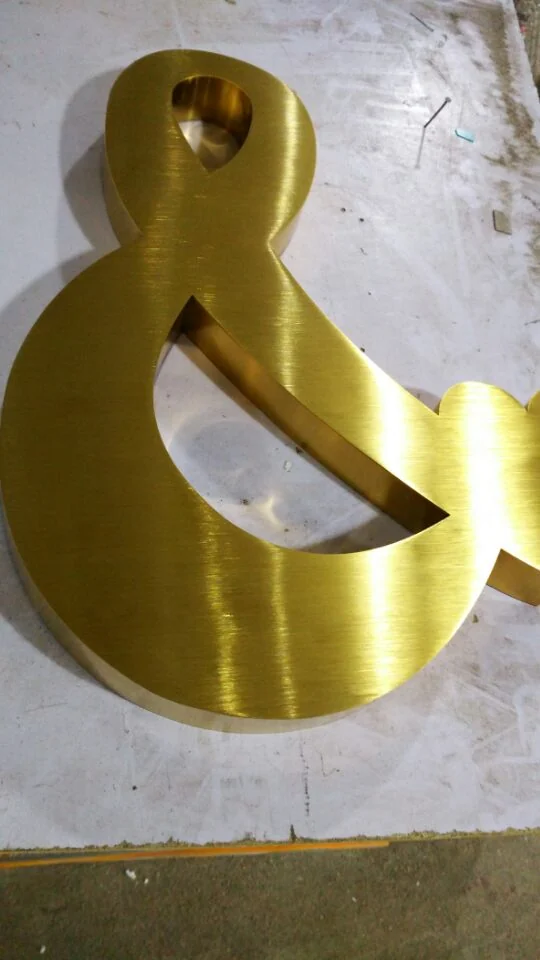 Gold-toned ampersand lying on a work surface, showing directional face texture and a deep side return.