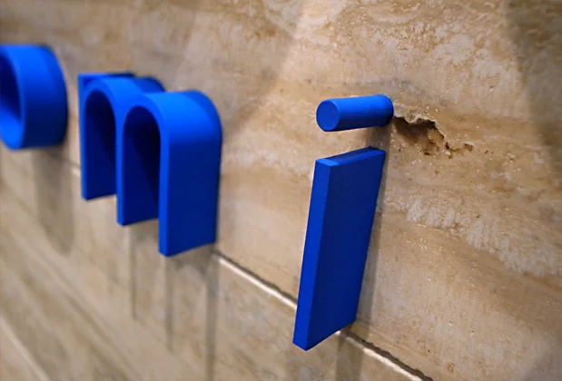Blue dimensional lowercase letters held away from a textured stone wall, with a visible gap and shadows.