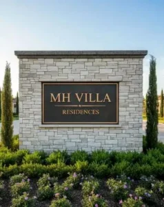 Low monument sign integrated into a stone entrance wall with landscaping.