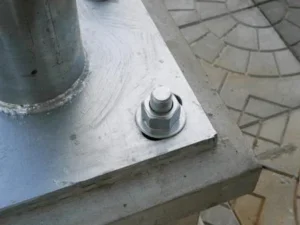 Close-up of a round steel post welded to a base plate and secured with an anchor bolt.